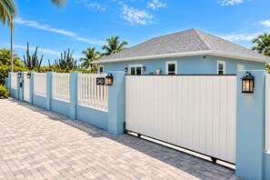 A light blue building with a gated entrance, a paved driveway, and a clear sky.