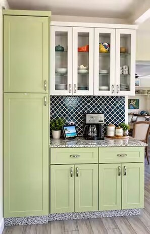 A kitchen with green cabinets, a coffee maker, and a potted plant on the counter.