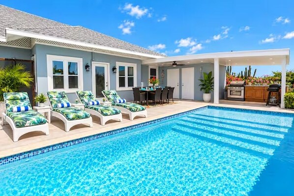 A swimming pool with lounge chairs, a barbecue area, and a covered patio.