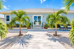 A house with a concrete driveway, palm trees, and a clear blue sky. - Baby Beach Bliss Aruba | Private Pool & Outdoor Kitchen | Walk to Baby Beach (San Nicolas)