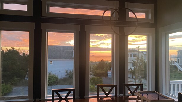 Ein Zimmer mit großen Fenstern und Blick auf einen Sonnenuntergang über einer Wohngegend.