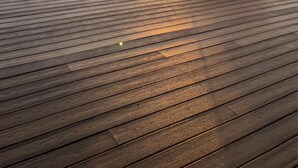 Eine Holzterrasse mit Stühlen und Geländer mit Blick auf ein Gewässer bei Sonnenuntergang.