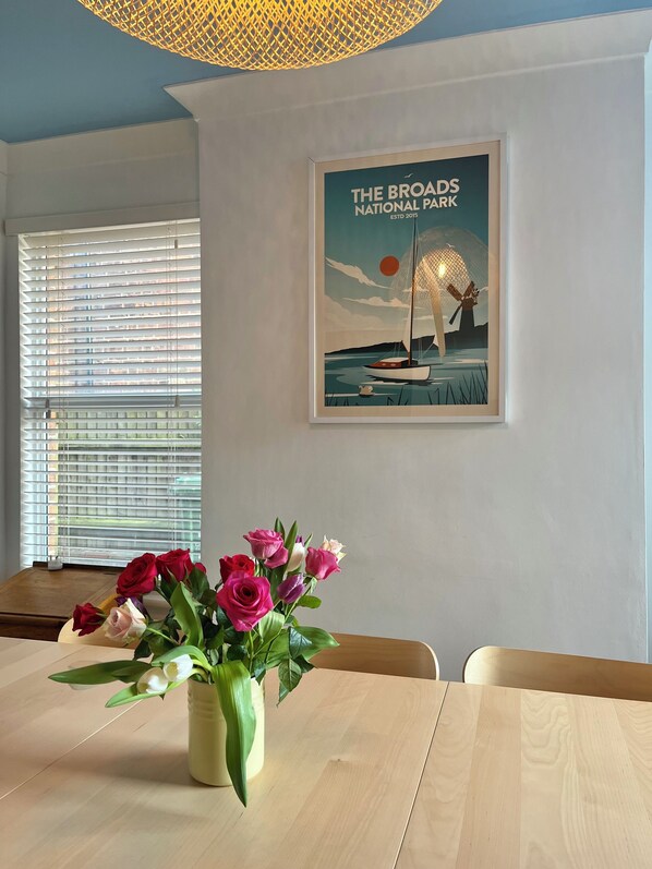 A dining area with a table, chairs, a vase of flowers, and a framed picture on the wall.
