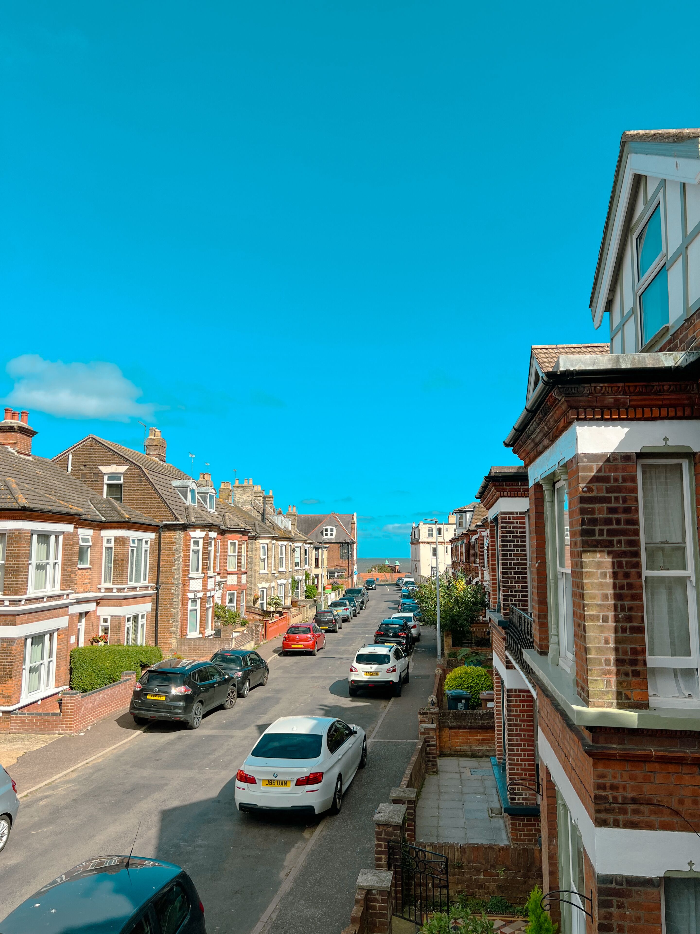A residential street with terraced houses, parked cars, and a clear blue sky.