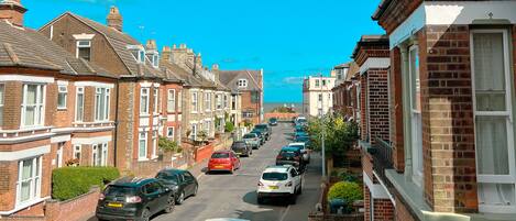 A residential street with terraced houses, parked cars, and a clear blue sky.