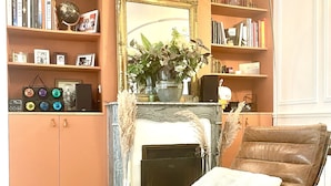 A cozy living room with a leather armchair, a fireplace, bookshelves, and a large mirror. - Gorgeous 5 Bedroom Parisian Home (Paris)