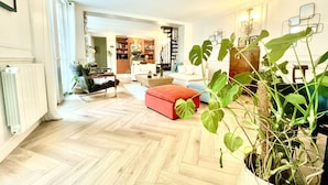 A spacious living room with a herringbone floor, a red sofa, and a large potted plant. - Gorgeous 5 Bedroom Parisian Home (Paris)