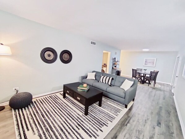 A living room with a sofa, coffee table, and a dining area with chairs and a table.