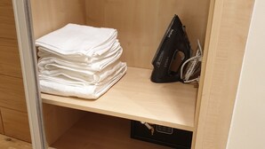 Une armoire en bois, avec une pile de serviettes blanches, un fer à repasser noir et une corde enroulée.