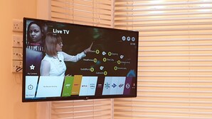 Un téléviseur à écran plat fixé au mur affiche une interface de télévision en direct avec différentes options de chaînes et une carte du Royaume-Uni.