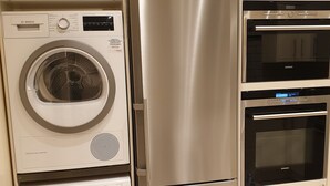 Une cuisine compacte équipée d’un réfrigérateur en acier inoxydable, d’un four encastré et d’un lave-linge.