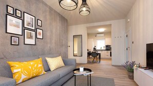 A modern living room with a grey sofa, yellow pillow, framed pictures on the wall, and a small table with a remote control. - Holiday apartment modernly furnished with swimming pool (Krk)