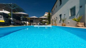A clear blue swimming pool with lounge chairs and umbrellas, surrounded by buildings with windows and potted plants. - Holiday apartment modernly furnished with swimming pool (Krk)