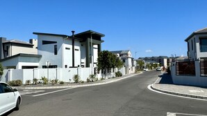 A modern residential street with contemporary houses, a clear sky, and a white car parked on the side. - Captivating Home with Mountain Views/Proximity to the Beach Your Perfect Getaway (Cape Town)