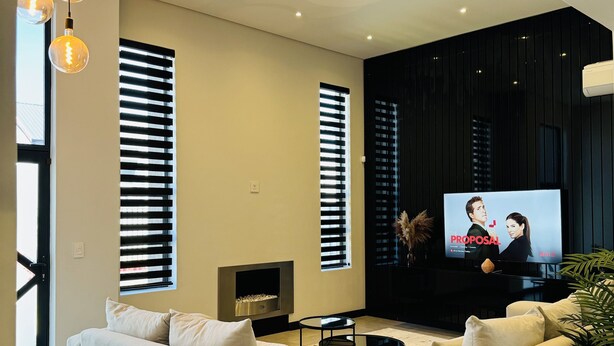 A modern living room with a large flat-screen TV, beige sofas, and a fireplace. - Captivating Home with Mountain Views/Proximity to the Beach Your Perfect Getaway (Cape Town)