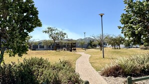 A paved pathway leading to a building with a covered outdoor area, surrounded by greenery and a clear sky. - Captivating Home with Mountain Views/Proximity to the Beach Your Perfect Getaway (Cape Town)