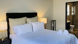 A neatly made bed with white linens and pillows, a bedside lamp, and a small table with a lamp. - Captivating Home with Mountain Views/Proximity to the Beach Your Perfect Getaway (Cape Town)