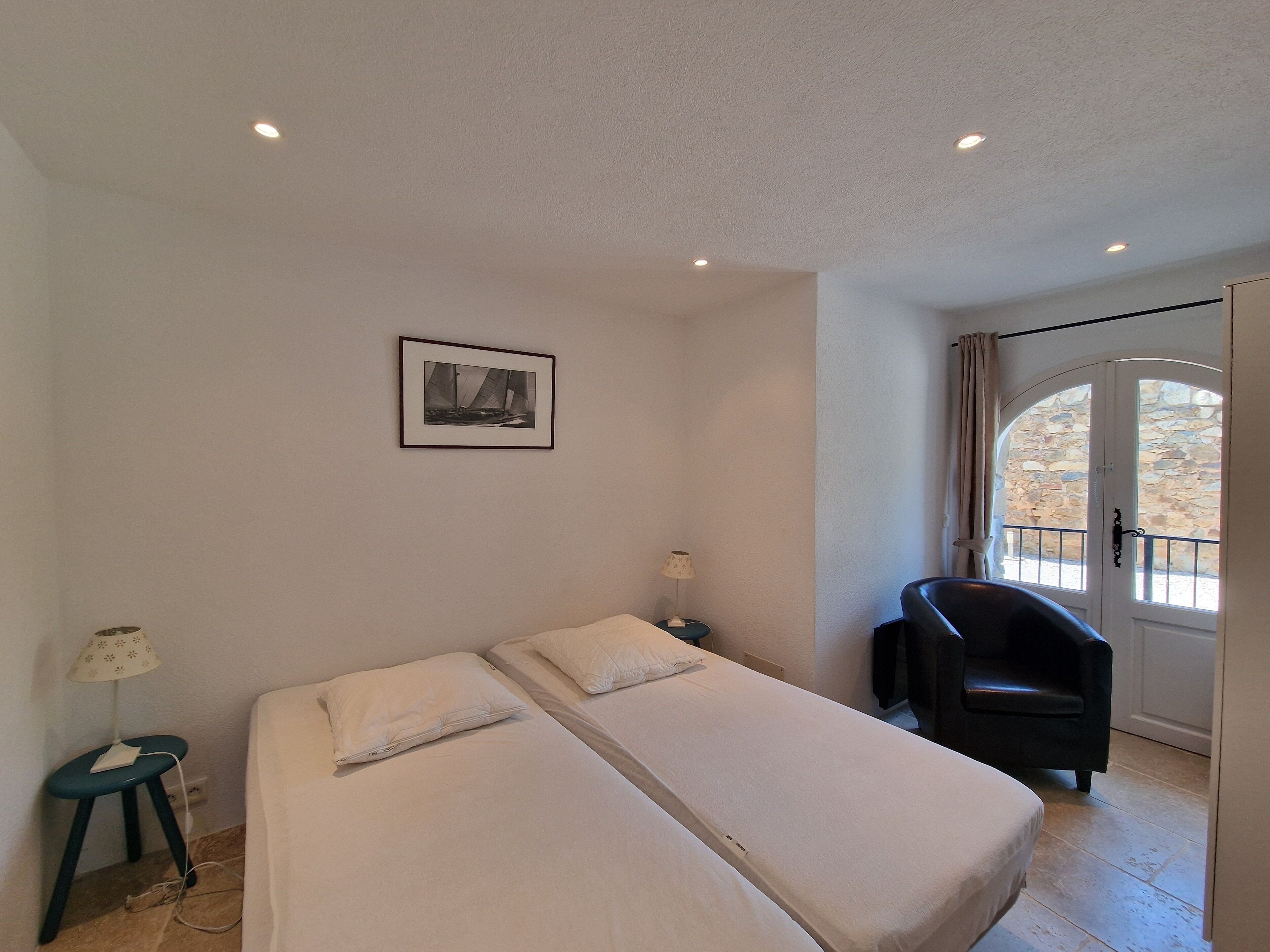 Une chambre d’hôtel avec deux lits simples, un bureau avec une chaise, une petite table avec une lampe et un tableau au mur.