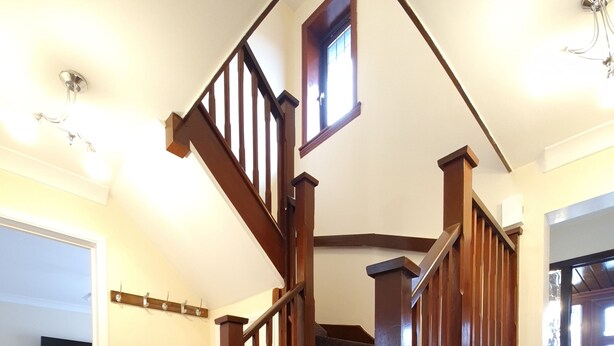 Eine Holztreppe mit einem dunklen Teppich und einem kleinen Fenster am Obergeschoss.