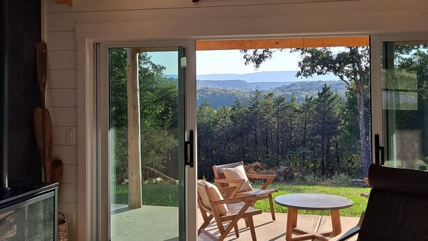 Ein geräumiger Wohnbereich mit großem Fenster und Blick auf eine reizvolle Landschaft, einem Kamin und einem Esstisch mit Sitzgelegenheiten im Freien.
