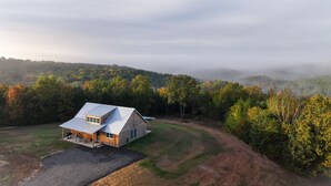 Ein modernes Haus mit einer Metallbedachung, umgeben von einer grünen Fläche und dichten Bäumen.