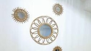 Una habitación con pared blanca, un espejo redondo y tres adornos en forma de sol. Hay una mesita con dos velas y una caja de pañuelos.