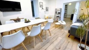 Una sala de estar moderna con un sofá blanco, una mesa de comedor con sillas y una planta grande en maceta.
