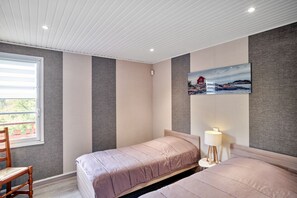 A bedroom with two beds, a window with blinds, a chair, and a painting on the wall.
