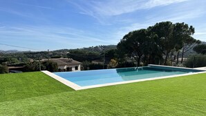 A rectangular swimming pool with a clear blue water surface, surrounded by a well-maintained green lawn. - Villa Cabañas with infinity pool, gardens and barbecue in Calonge, Costa Brava (Calonge)