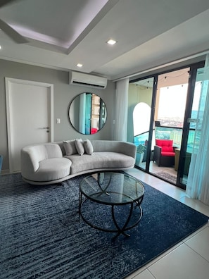 A modern living room with a curved sofa, a glass coffee table, and a large mirror.