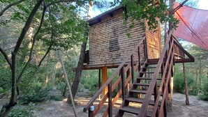 A wooden treehouse with a staircase and a red canopy. - TreeHouses Ljubač Glamping Robinson (Razanac)