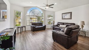 A spacious living room with a large arched window, a ceiling fan, and leather sofas.