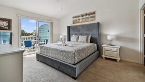 A bedroom with a large bed, a nightstand, a ceiling fan, and a view of the outdoors.
