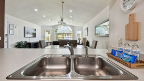 A modern kitchen with a double sink, a wooden cutting board, and a clock on the wall.