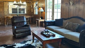 Un intérieur rustique avec des murs en bois, un fauteuil en cuir, un canapé, une table basse et un tapis en peau de vache.