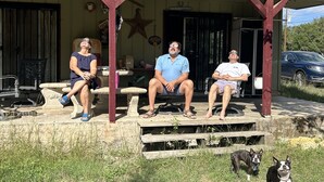 Trois personnes sont assises sur un porche doté d’un toit, décoré d’une étoile, et un chien se trouve au premier plan.