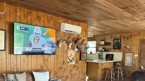 L’intérieur d’un chalet rustique est agrémenté d’un canapé en cuir, d’un tapis en peau de vache noir et blanc, d’un coin repas en bois et d’une tête de cerf fixée au mur.