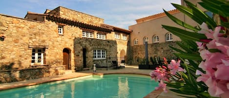A stone building with a swimming pool, arched windows, and a tiled roof.
