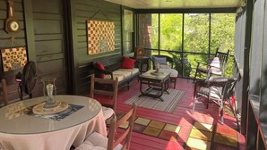 Eine überdachte Veranda mit Korbmöbeln, einem Tisch mit Glasplatte und Blick ins Grüne.