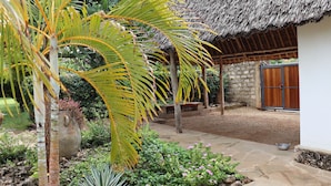 Un jardín con una estructura de techo de paja, sendero de piedra y diversas plantas.