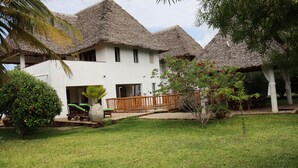 Una cabaña con techos de paja, una terraza de madera y un jardín con plantas tropicales.