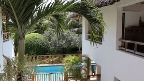 Zona junto a la piscina con cerca de madera, una palmera y vistas a un jardín exuberante.