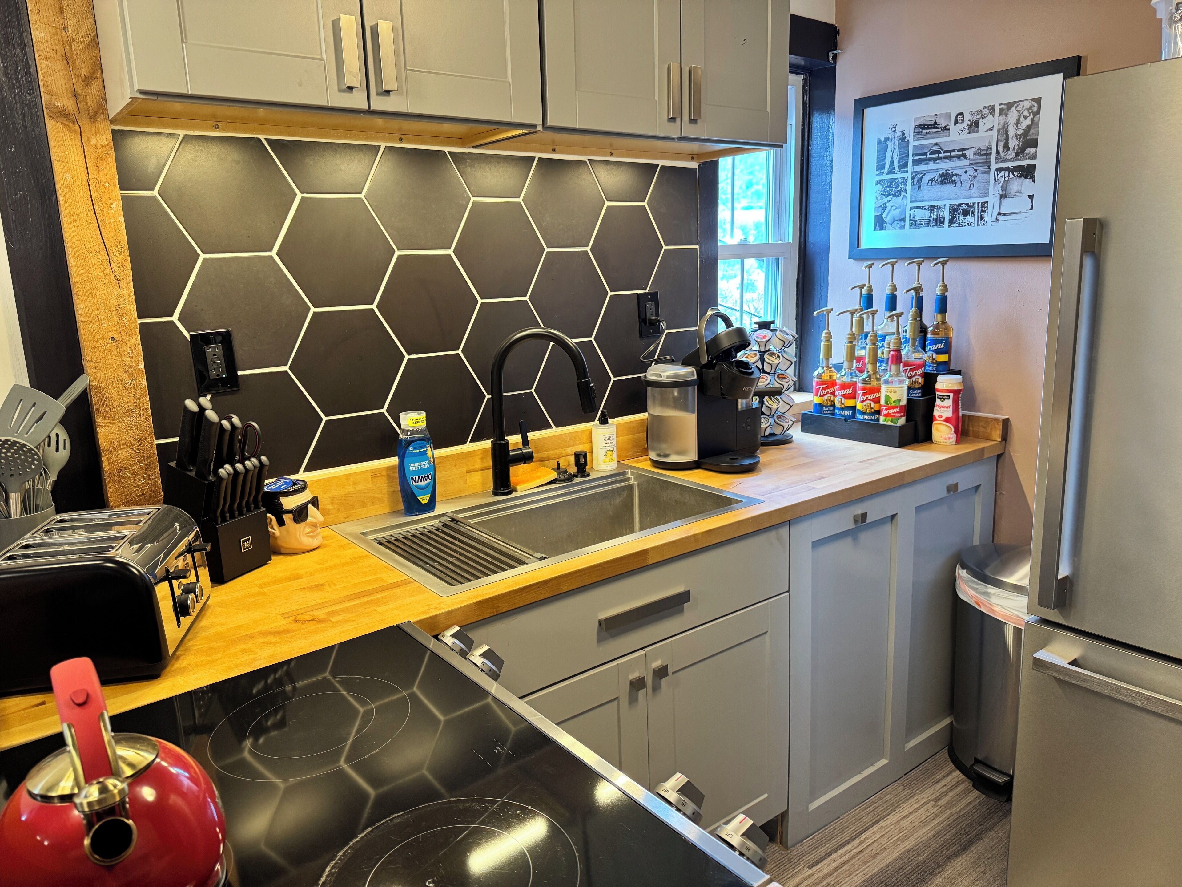 Cozinha moderna com painel hexagonal preto, eletrodomésticos de aço inoxidável e bancada de madeira.