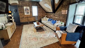 A cozy living room with a brick wall, a ceiling fan, a sofa, a coffee table, and a rug. - Stylish, Historic PSU-themed Apt.—2 blocks from Waterfront (Bellefonte)