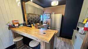 A modern kitchen with a wooden bar, two stools, a stainless steel refrigerator, and a hexagonal backsplash. - Stylish, Historic PSU-themed Apt.—2 blocks from Waterfront (Bellefonte)