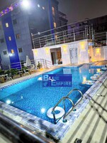 Piscina com design em mosaico azul, cercada por guarda-corpo de metal e um pequeno flutuador inflável.