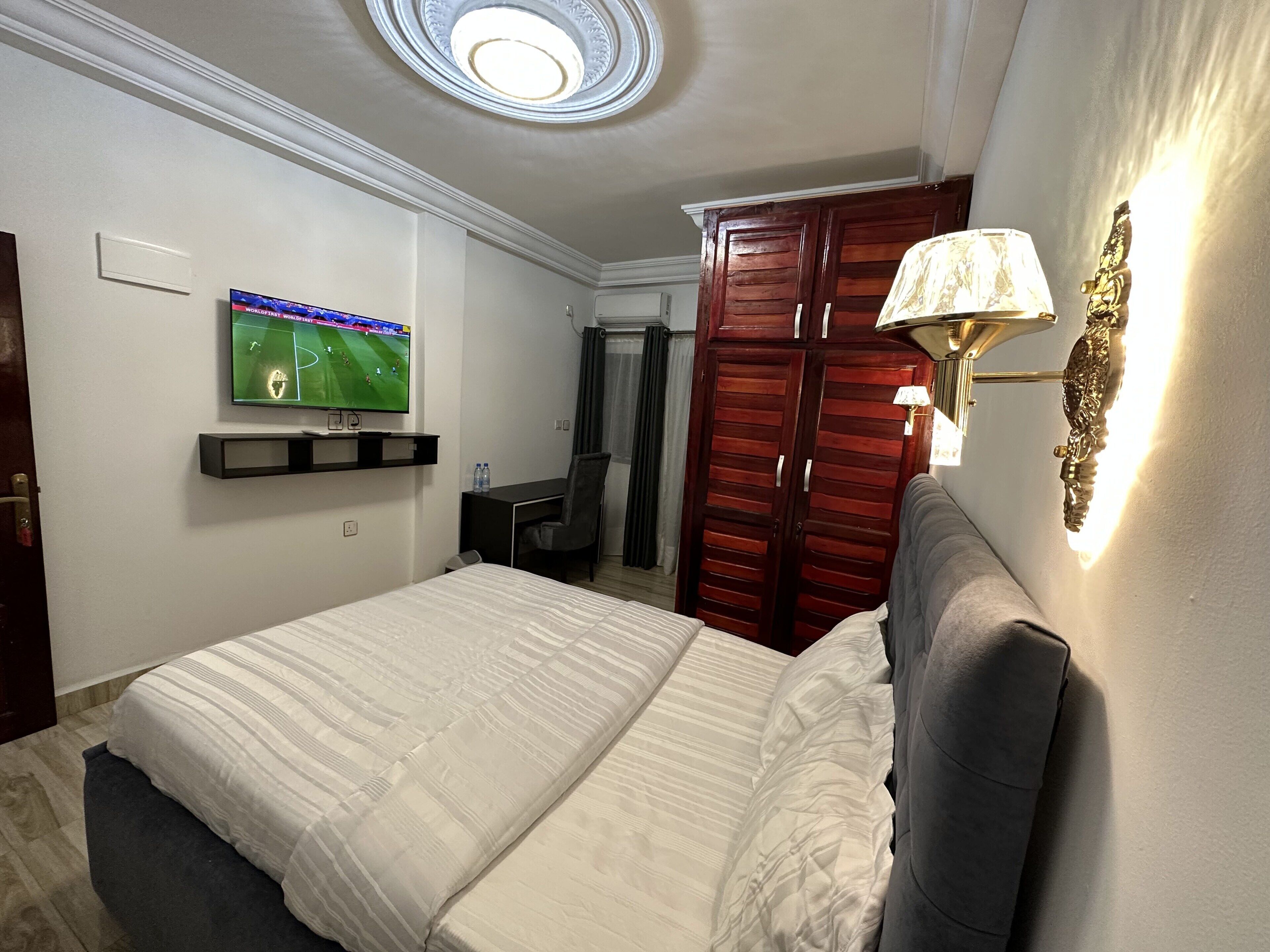 A hotel room with a bed, a desk, a TV mounted on the wall, and a wardrobe.