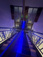 Escadaria moderna com iluminação azul, corrimãos de metal e barreira de vidro.
