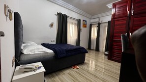 A hotel room with a bed, a desk with a phone, and a red door. - BLUE EMPIRE HOTEL (Buea)
