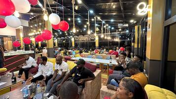 A spacious indoor venue with multiple seating areas, tables with drinks, and hanging decorations.